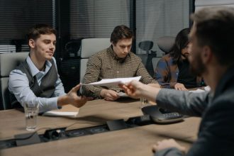 Quatro pessoas trocam documentos durante uma reunião em um escritório.