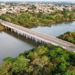 Vista aérea de uma ponte sobre um rio cercado por vegetação, em Cuiabá, Mato Grosso.