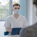 Profissional de saúde conversa com paciente e faz anotações durante atendimento clínico.